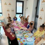 Detaliu cu mâinile unor copii care prepară frigărui de fructe proaspete (banane, căpșuni, struguri)