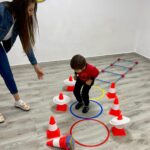 Copii făcând sărituri ghemuite prin cercuri colorate pentru antrenarea echilibrului.