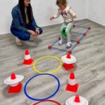 Copil de grădiniță sărind cu mingea între picioare la activitatea Micul Campion în mișcare.