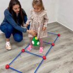 Copil de grădiniță sărind cu mingea între picioare la activitatea Micul Campion în mișcare.