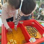 Copii căutând albinuțe ascunse într-o activitate educativă și senzorială la grădiniță.