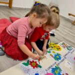 Copiii stau pe pernuțe și pictează flori de primăvară la Grădinița Don Castor