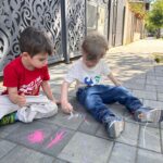 Copii desenând pe asfalt în curtea Grădiniței Don Castor din București în cadrul unei activități educative și recreative.